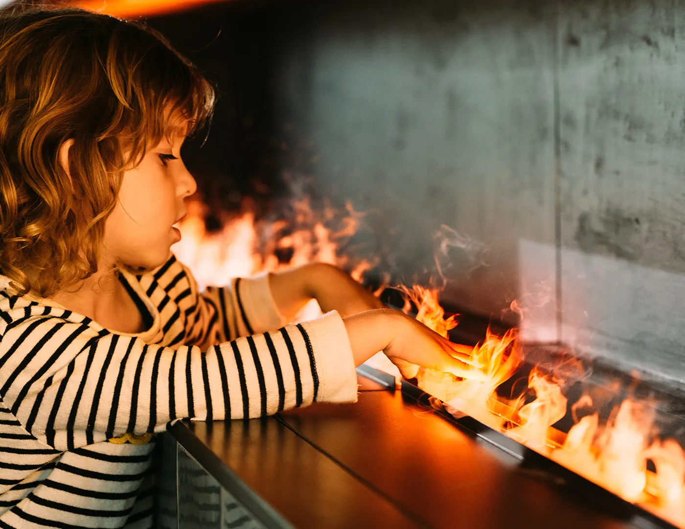 Kleines Mädchen mit ihren Fingern, die in eine Wasser-Dampf-Feuerstelle-Flamme stecken